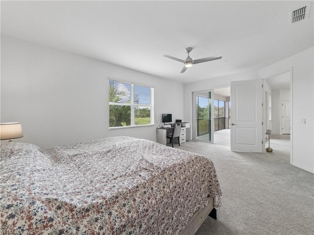 Bedroom with a floral-quilted bed, desk, ceiling fan, and sliding doors to a screened balcony.