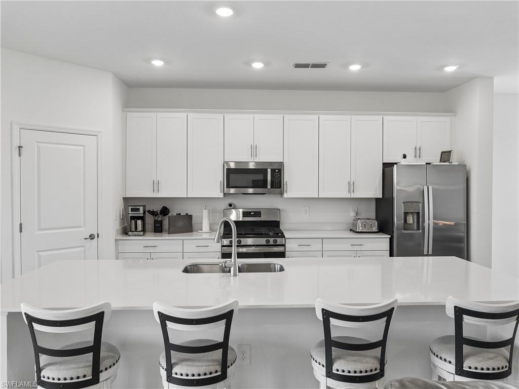Modern white kitchen with a large island, four bar stools, and stainless steel appliances.