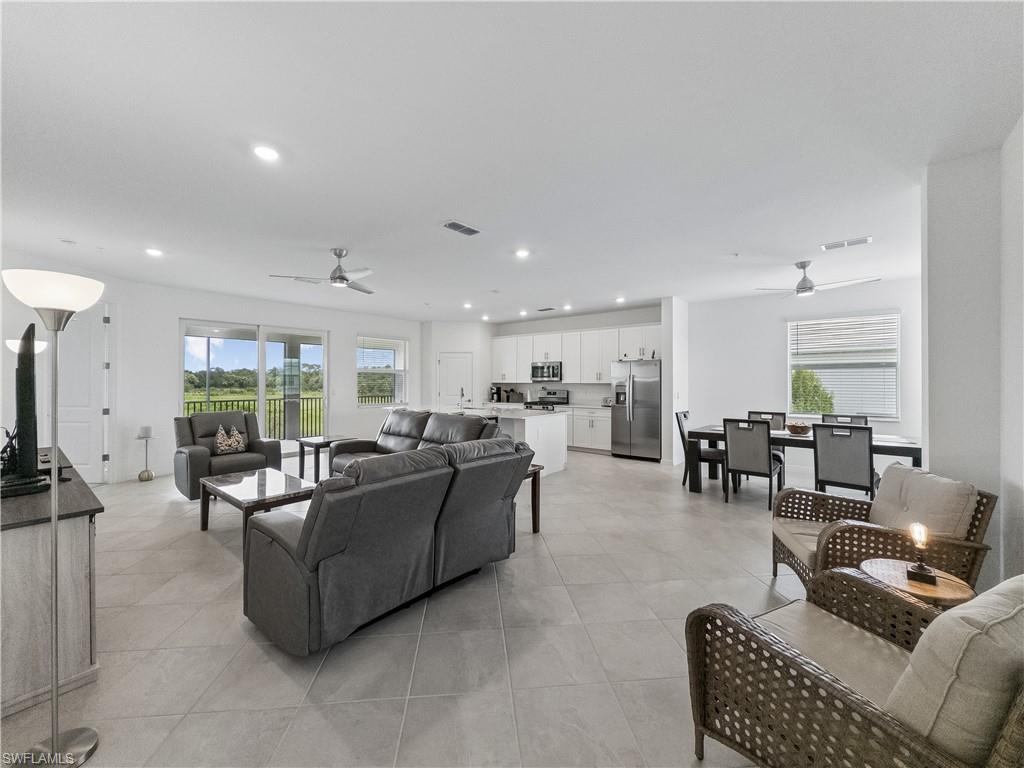 Open-plan living room with gray seating, white kitchen, dining area, and sliding glass doors to a balcony.