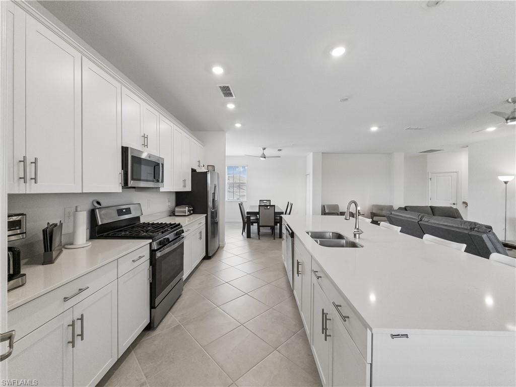Open-plan kitchen with white cabinets, stainless appliances, and a large island overlooking the dining and living areas.