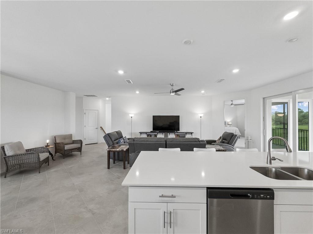 Open-plan living room and kitchen with a white island, gray seating, and sliding glass doors to greenery.