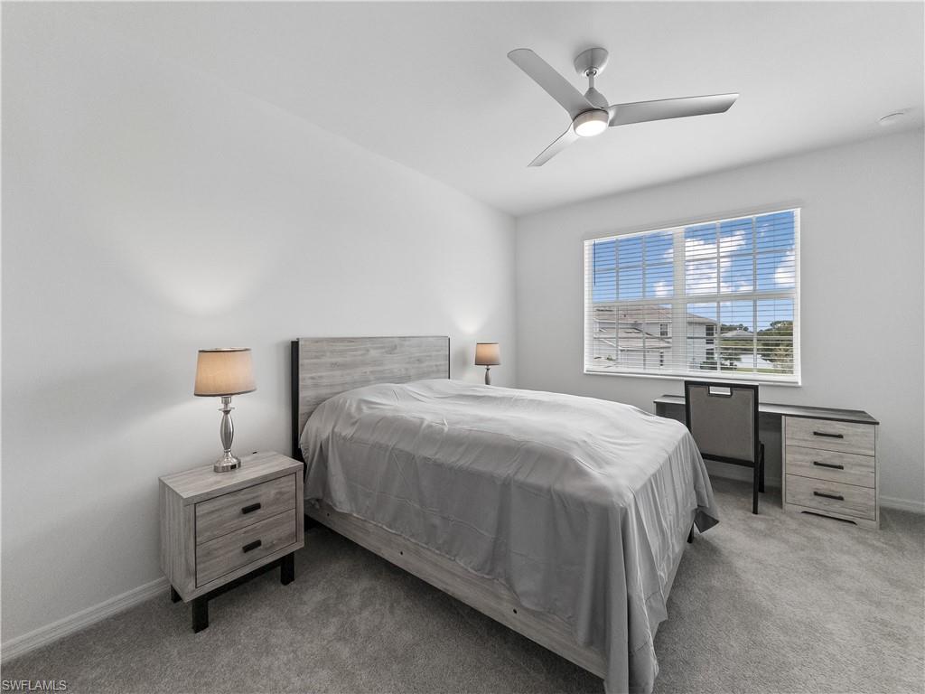 Bedroom with a gray bed and matching furniture, ceiling fan, and a window overlooking homes and water.