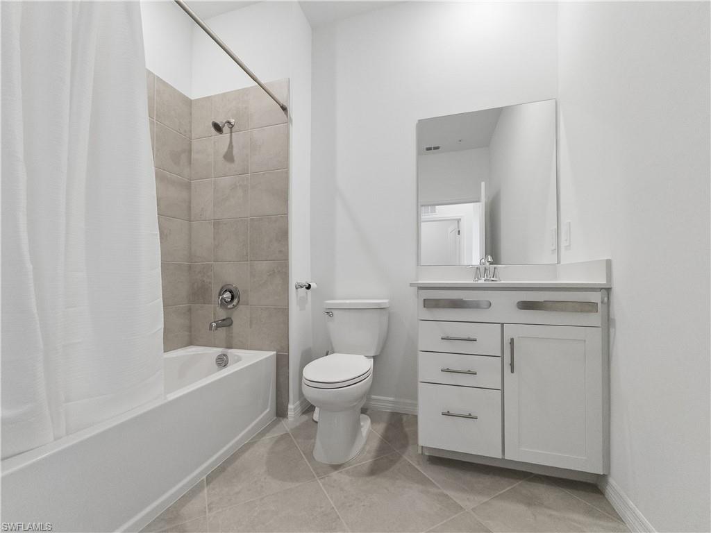 Bathroom with a curtained tub, beige tile, toilet, and white vanity with a large mirror.