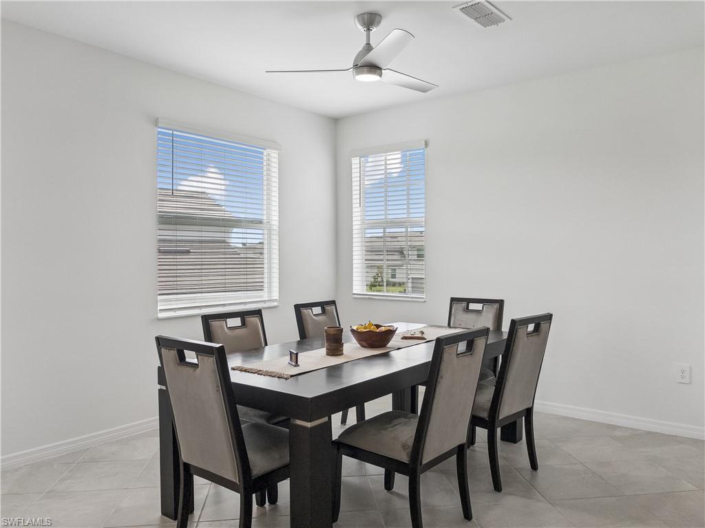 Dining room with a dark table, six upholstered chairs, two bright windows, and a ceiling fan.