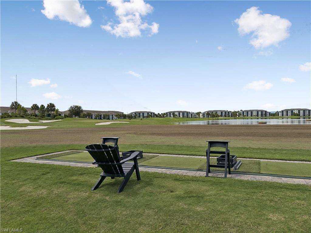 Golf course with a putting green, Adirondack chairs, lake, and distant residential buildings.