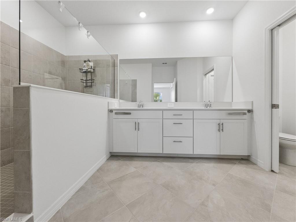Modern bathroom with a long double-sink vanity, gray tile floor, and glass-enclosed shower.