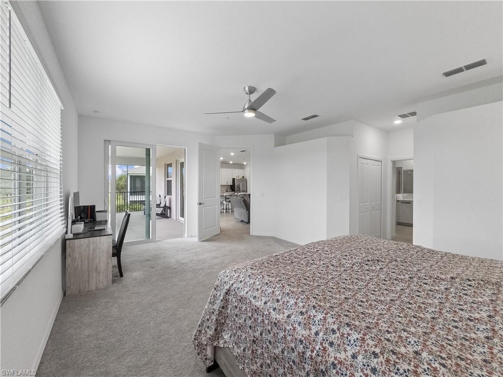 Bedroom with a patterned bedspread, desk by the window, and sliding doors to a balcony.