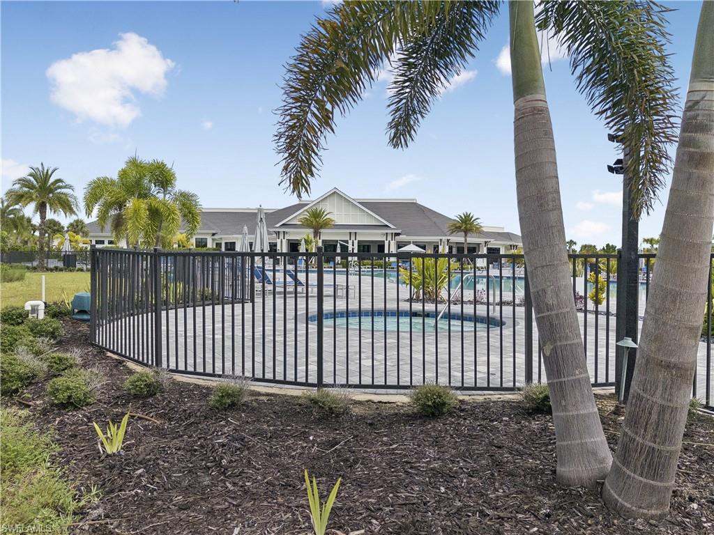 Community pool and clubhouse behind a black metal fence, framed by palm trees.