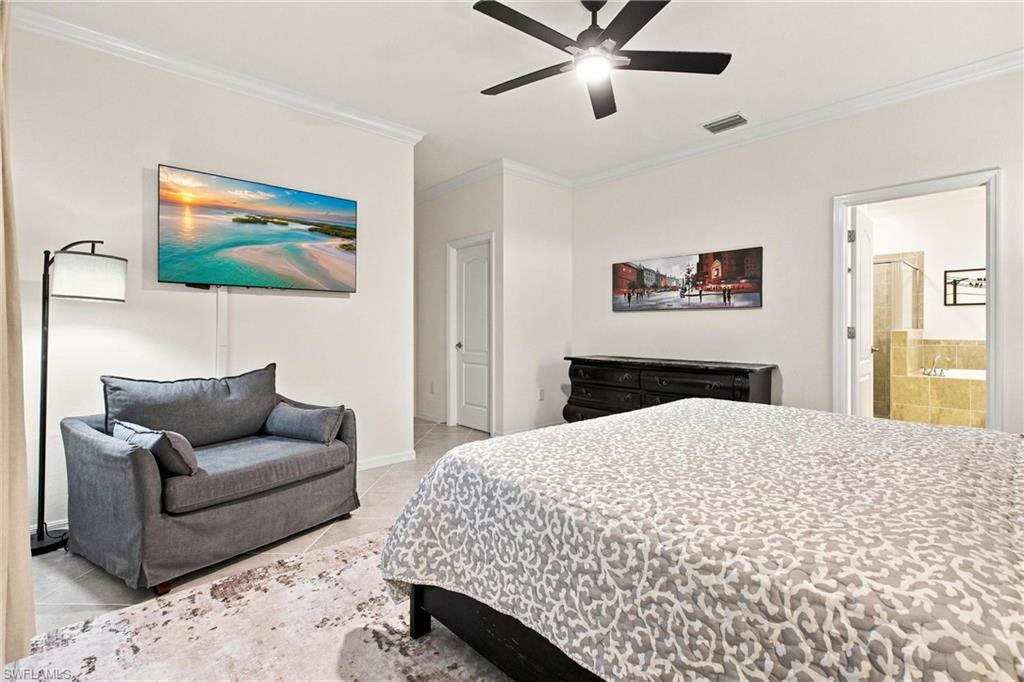 Furnished bedroom with a patterned bed, gray loveseat, and doorway to a tiled bathroom.