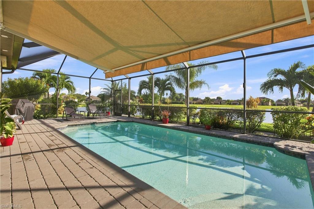 Swimming pool beneath a screened lanai, with a tan awning and lake view.