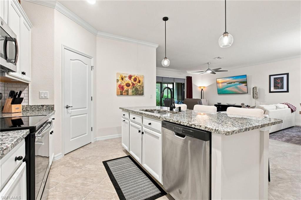 Open-plan kitchen with a granite island, stainless steel dishwasher, and adjoining white-furnished living room.