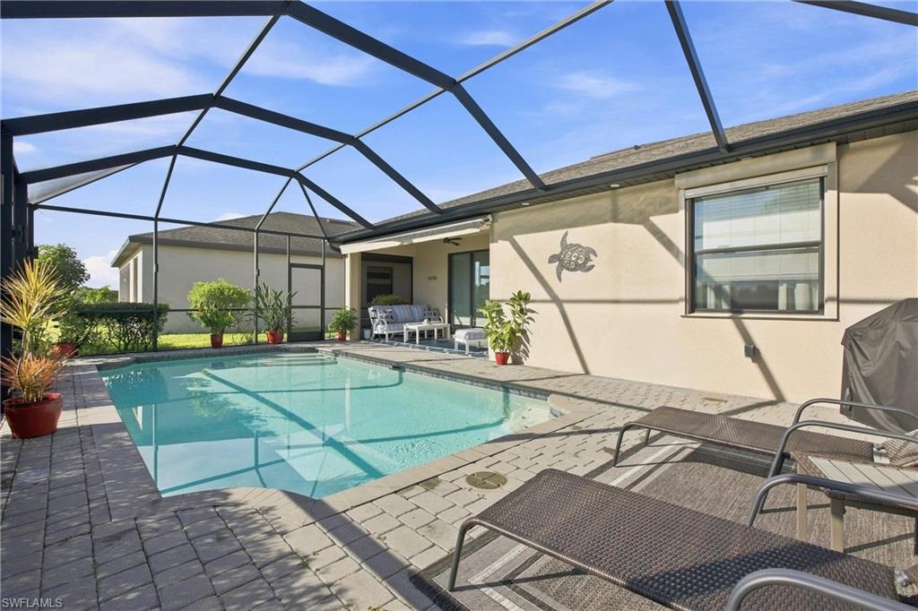 Backyard pool beside a beige home, with patio seating beneath a screened enclosure.