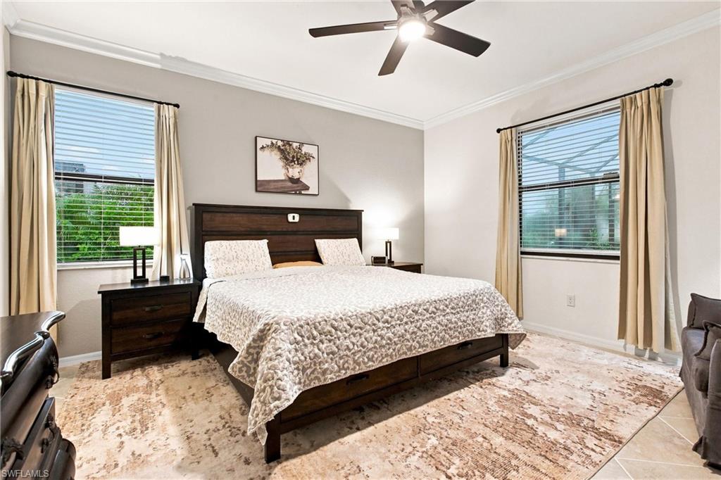 Furnished bedroom with a dark wood bed, cream bedding, two curtained windows, and a ceiling fan.