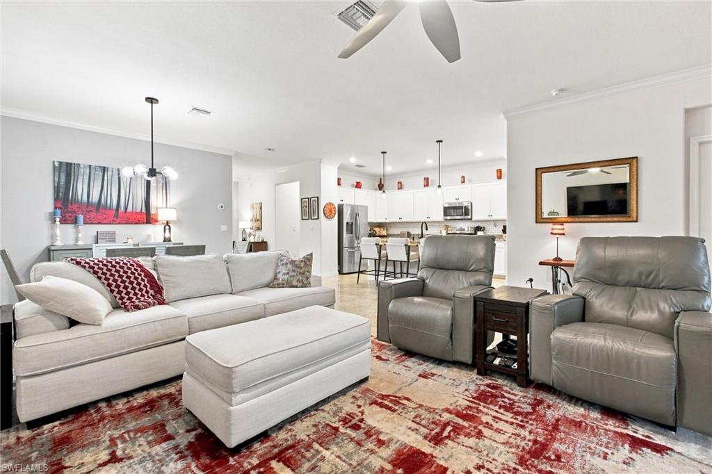 Living room with a light sectional, gray recliners, red-and-cream rug, and open kitchen.