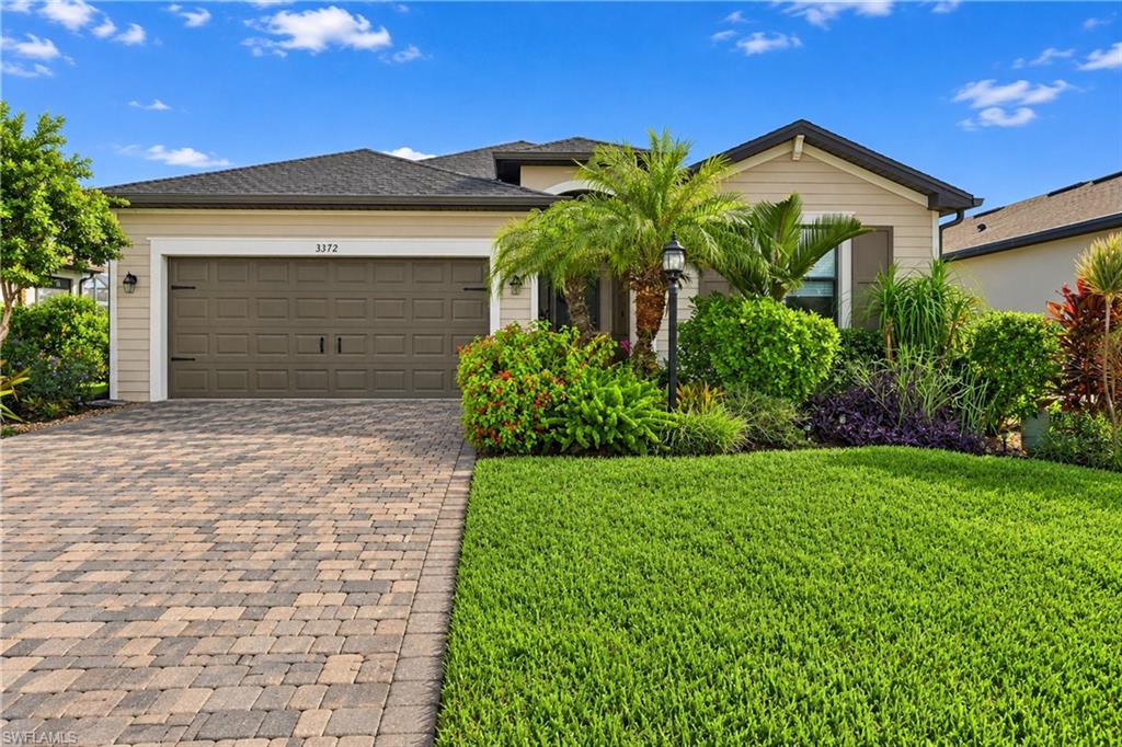 Single-story beige home with a double garage, paver driveway, palm trees, and manicured lawn.