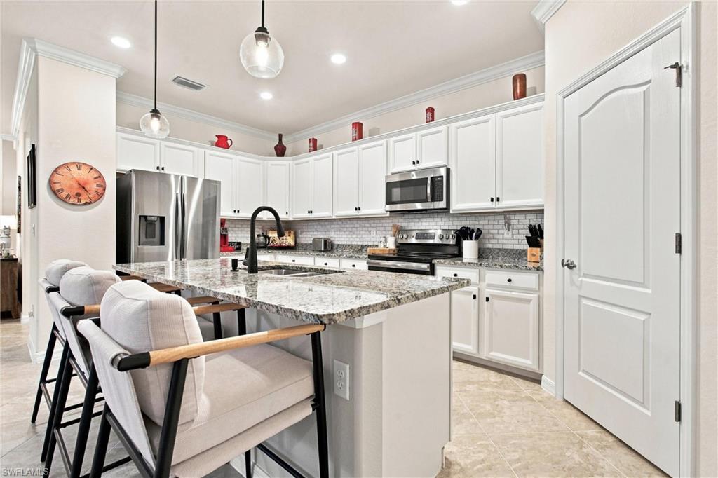 Kitchen with white cabinets, stainless steel appliances, and a granite island with seating.