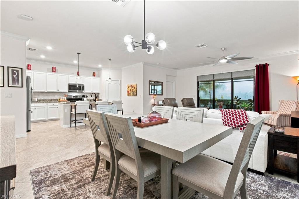 Open-plan dining area with a large gray table, white kitchen, and living room beside sliding glass doors.