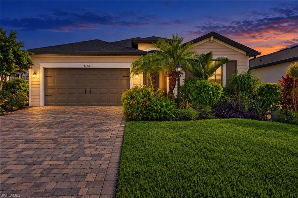 Single-story home with a two-car garage, paver driveway, and palms at dusk.
