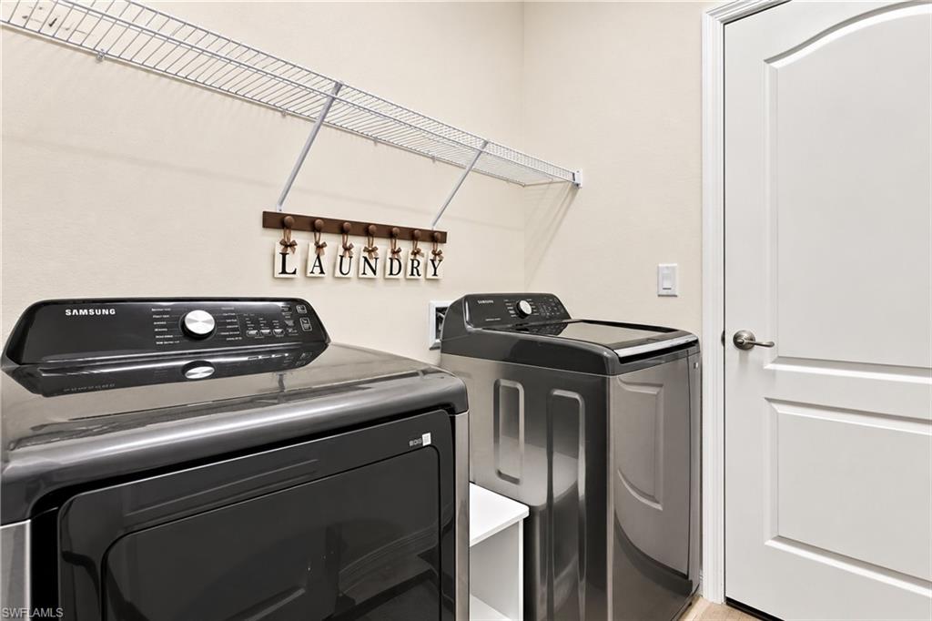 Laundry room with black washer and dryer beneath a wire shelf and laundry sign.