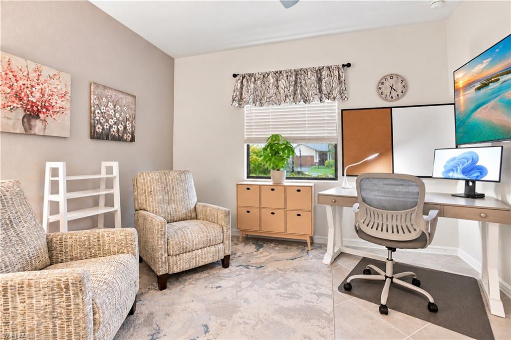 Furnished home office with a white desk, two patterned armchairs, and a window overlooking the yard.