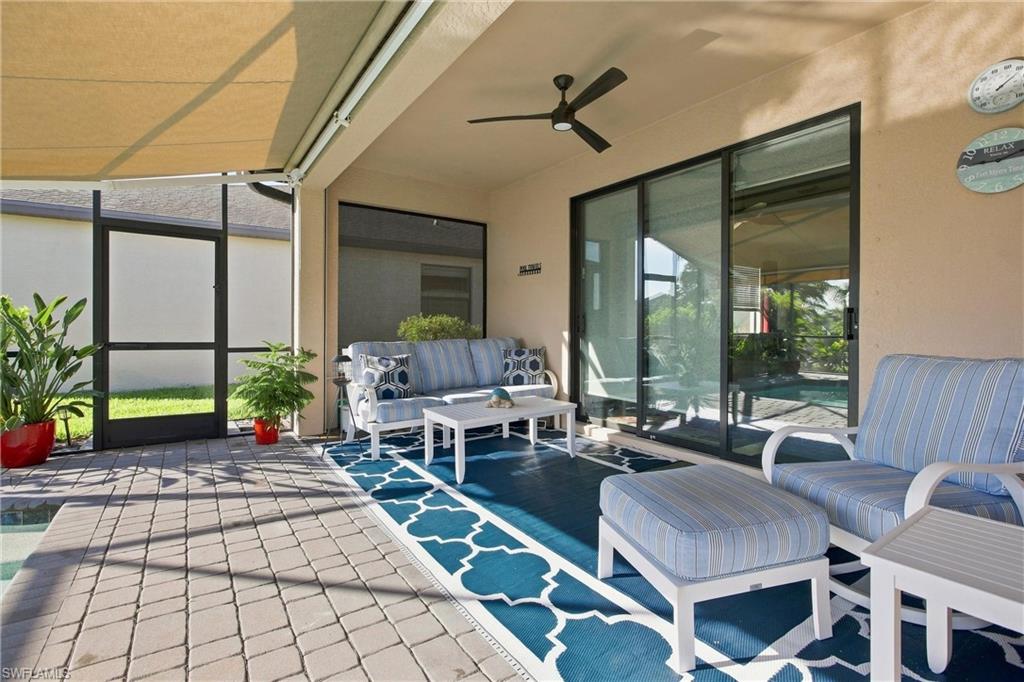 Screened lanai with blue-and-white seating, a ceiling fan, and a retractable shade.