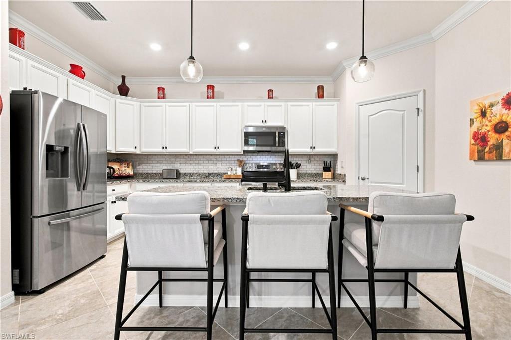 Kitchen with white cabinets, stainless appliances, and a stone island with three bar stools.