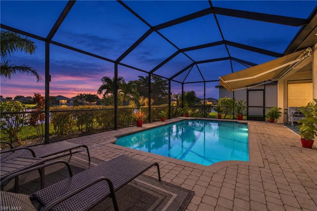 Screened pool lanai at dusk with lounge chairs and a pink sunset beyond the enclosure.
