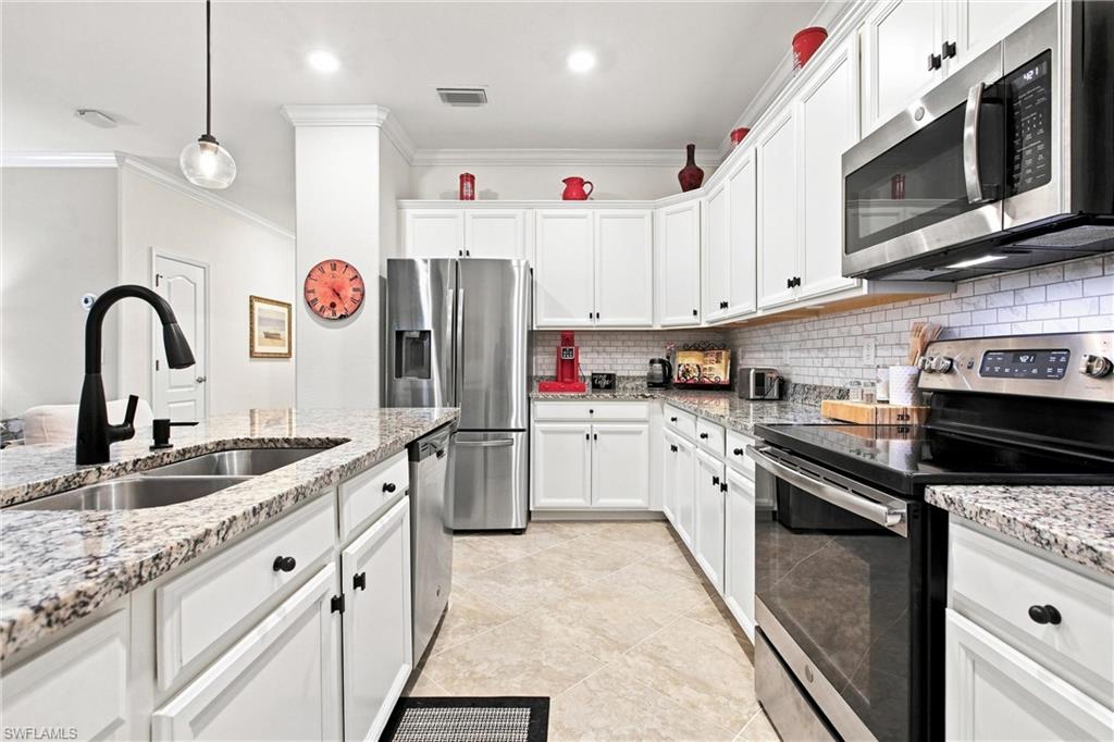 Bright white kitchen with granite island, double-basin sink, and stainless steel appliances.