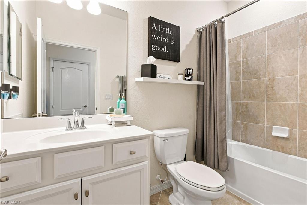Bathroom with a white vanity, toilet, and beige-tiled tub behind a taupe curtain.
