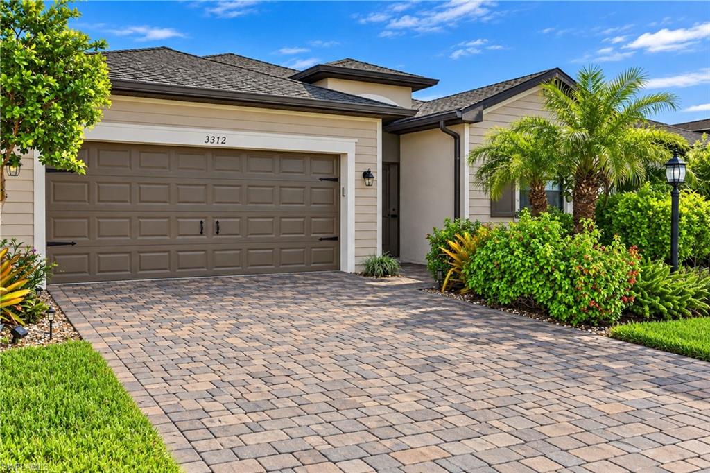 Home exterior with a double garage, paver driveway, and tropical landscaping.