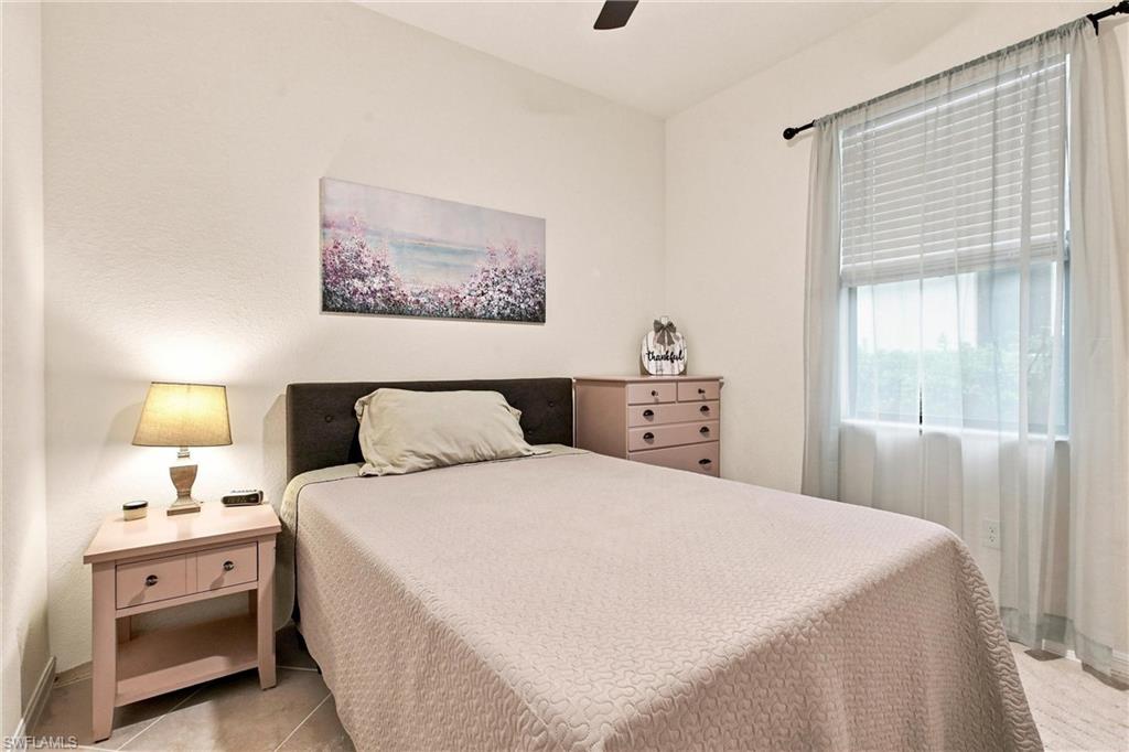 Furnished bedroom with a large bed, dark headboard, pink furniture, and a bright window with sheer curtains.