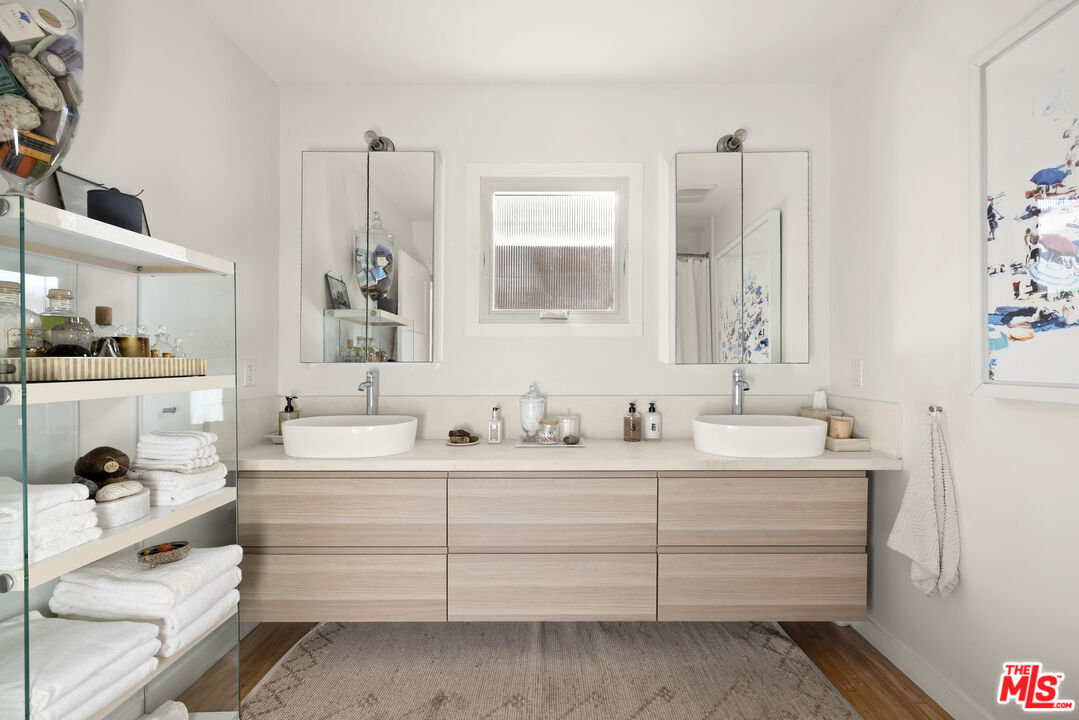 Bathroom with a double vanity, vessel sinks, mirrored cabinets, and open glass shelving.