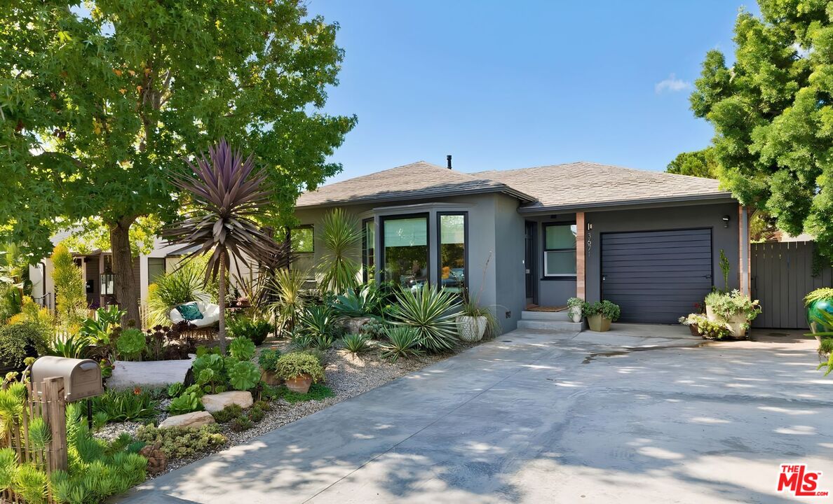 Gray single-story home with an attached garage and a lush, drought-tolerant front garden.