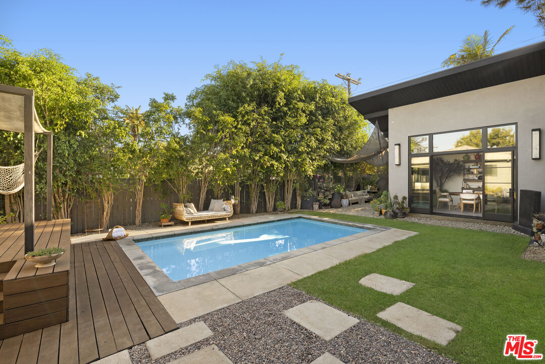 Backyard pool beside a modern home, with a wood deck, lawn, and shaded seating.