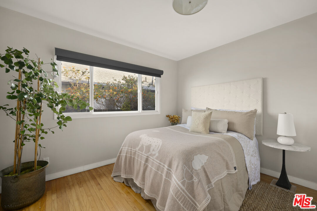 Bedroom with a neatly made bed, large window, and potted plant.
