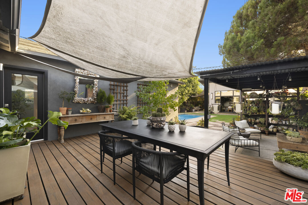Outdoor dining deck beneath a shade sail, with a swimming pool and covered garden seating.