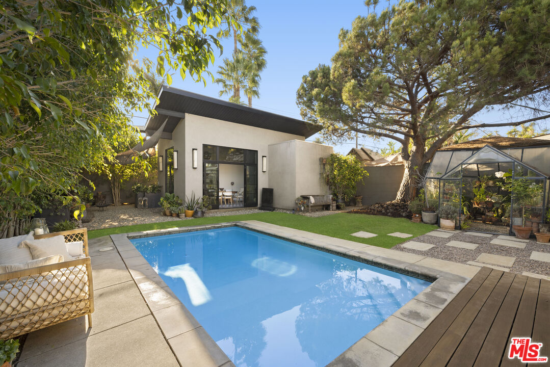Backyard pool beside a modern home, with a greenhouse and mature trees.