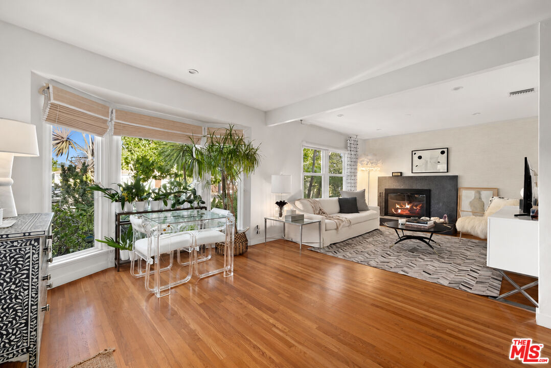 Living room with a fireplace, hardwood floors, and a glass dining table beside large windows.