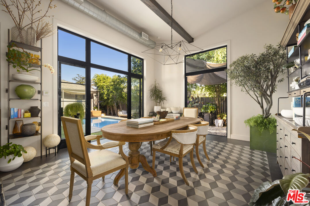 Dining room with geometric tile floors, an oval wood table, and black-framed windows overlooking a pool and garden.