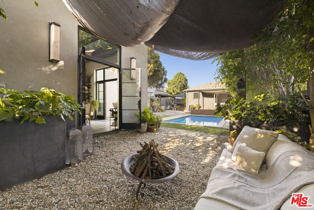 Gravel courtyard with a fire pit and outdoor sofa, looking toward a swimming pool.