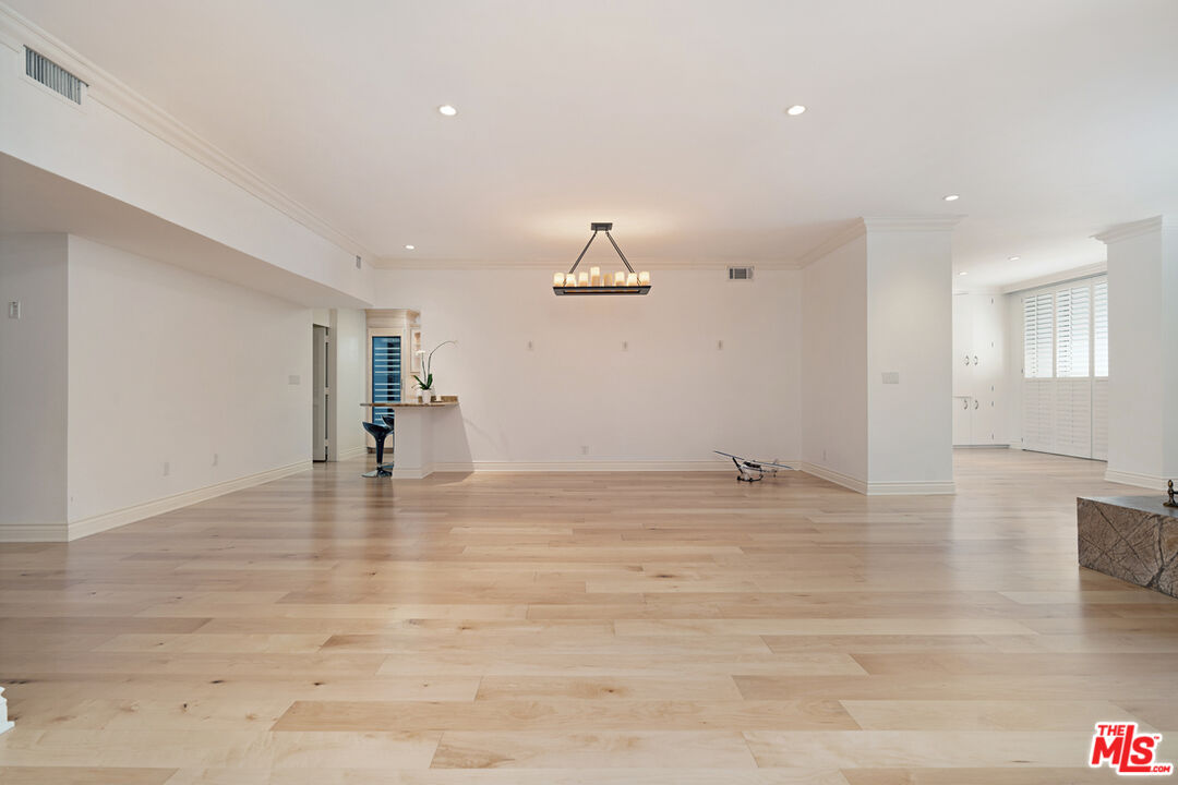 Open living and dining area with pale hardwood floors, a modern chandelier, and shuttered windows.