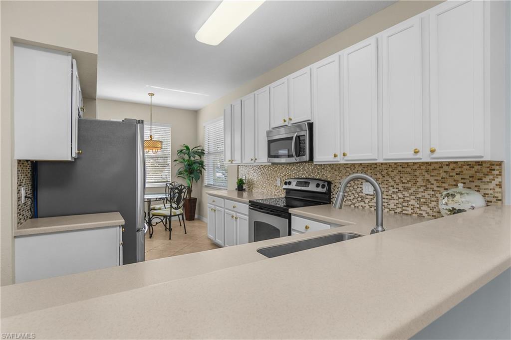 Kitchen with white cabinets, mosaic backsplash, stainless appliances, and a window-side breakfast nook.
