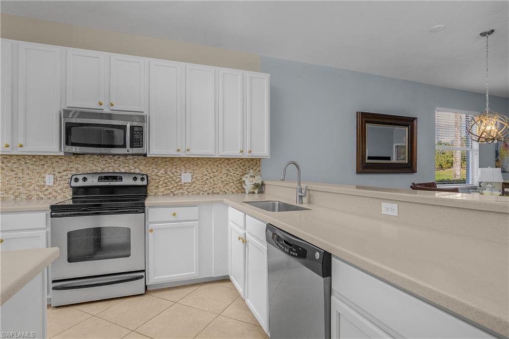 Kitchen with white cabinets, stainless appliances, mosaic tile backsplash, and a long breakfast bar.