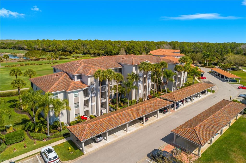 Aerial view of condominium buildings, carports, palms, and golf course; red arrow marks a unit.