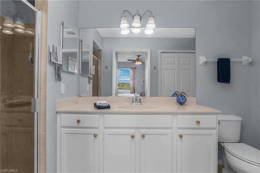Bathroom with a white vanity and large mirror, glass-enclosed shower, and toilet.