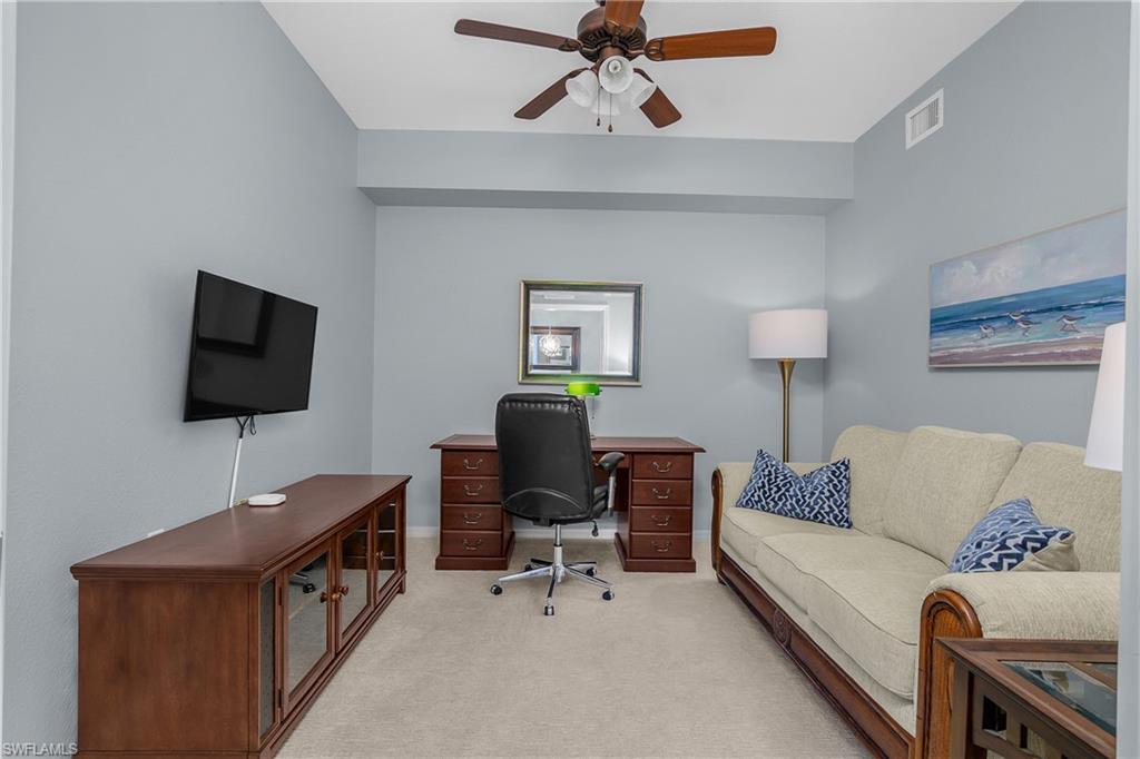 Furnished den with a wooden desk, wall-mounted TV, and beige sofa.
