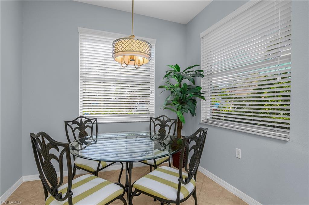 Dining nook with a round glass table, striped chairs, white blinds, and a pendant light.