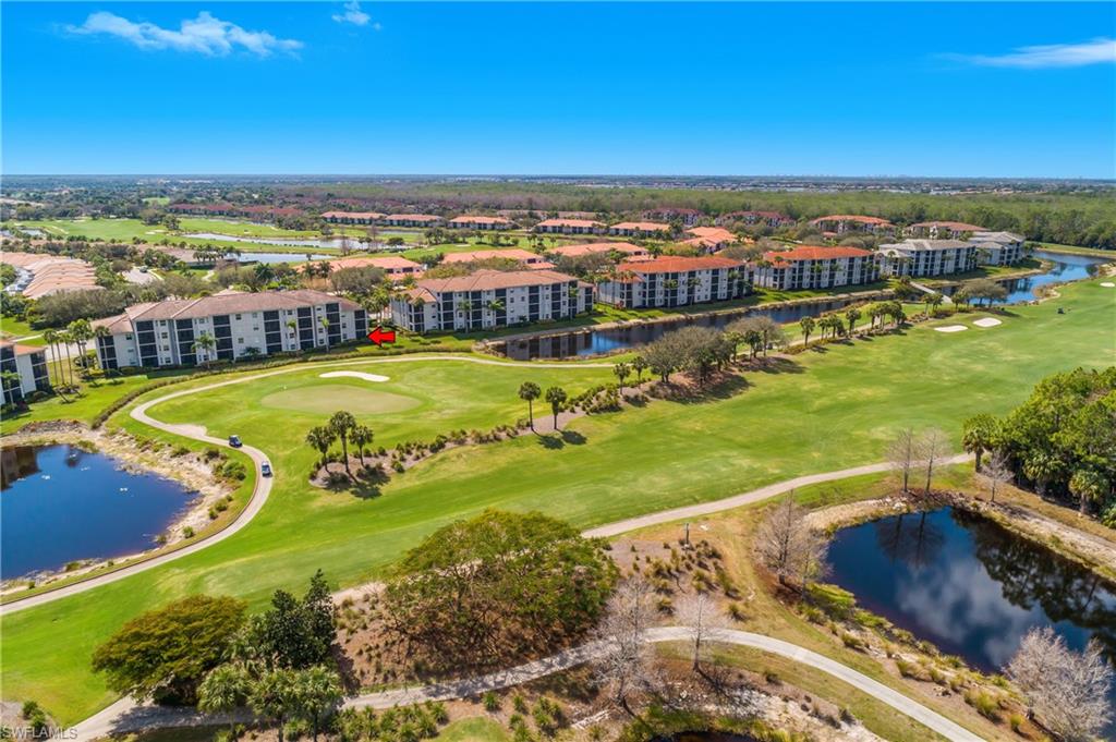 Aerial view of golf course and ponds beside multi-story residential buildings with terracotta roofs.