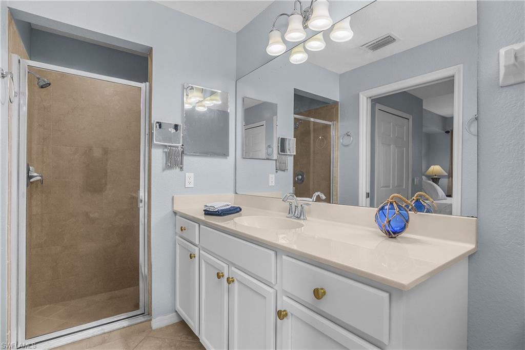 Bathroom with a long white vanity, wide mirror, and glass-enclosed tan-tile shower.