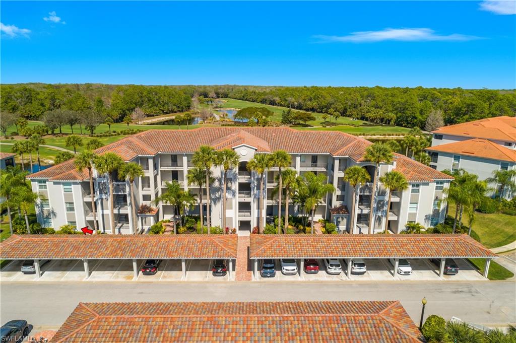 Aerial view of a palm-lined condominium building with covered parking and a golf course behind it.